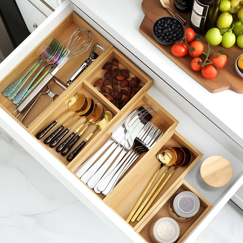 Bamboo drawer organizer trays holding cutlery and kitchen utensils in a white kitchen drawer