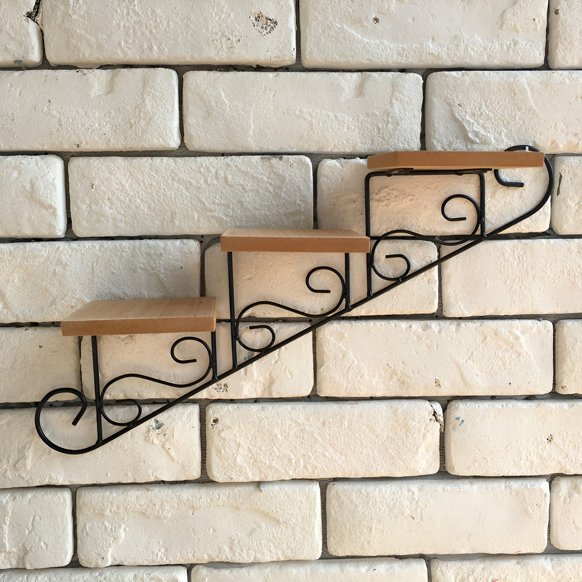 Empty wrought iron stair-step wall shelf with scrolled metal frame and three wood shelves on a white brick wall